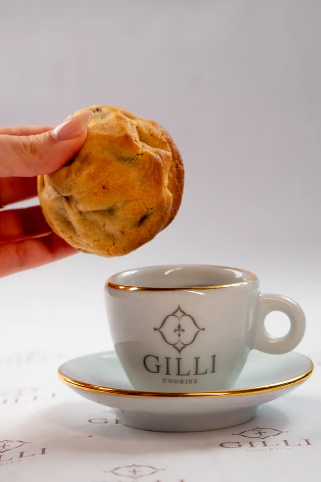 Cookie Gilli sendo mergulhado em uma xícara de café com o brasão