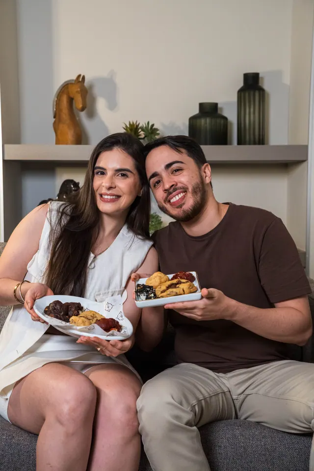 Ítalo e Gabi, fundadores da Gilli, sentados no sofá segurando pratos com cookies
